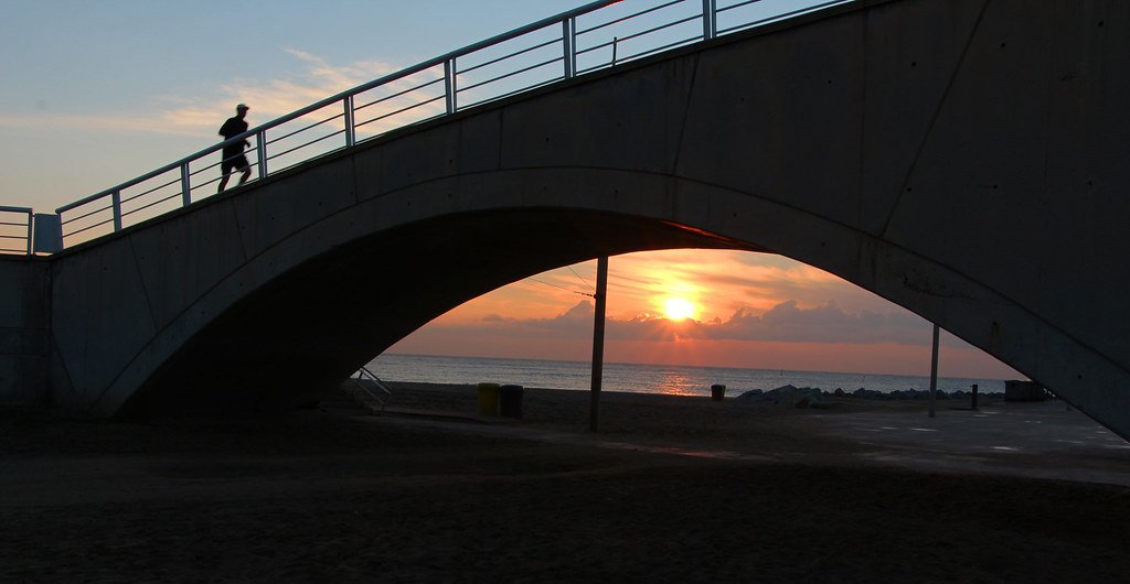 Corredor cruzando un puente junto al mar al amanecer